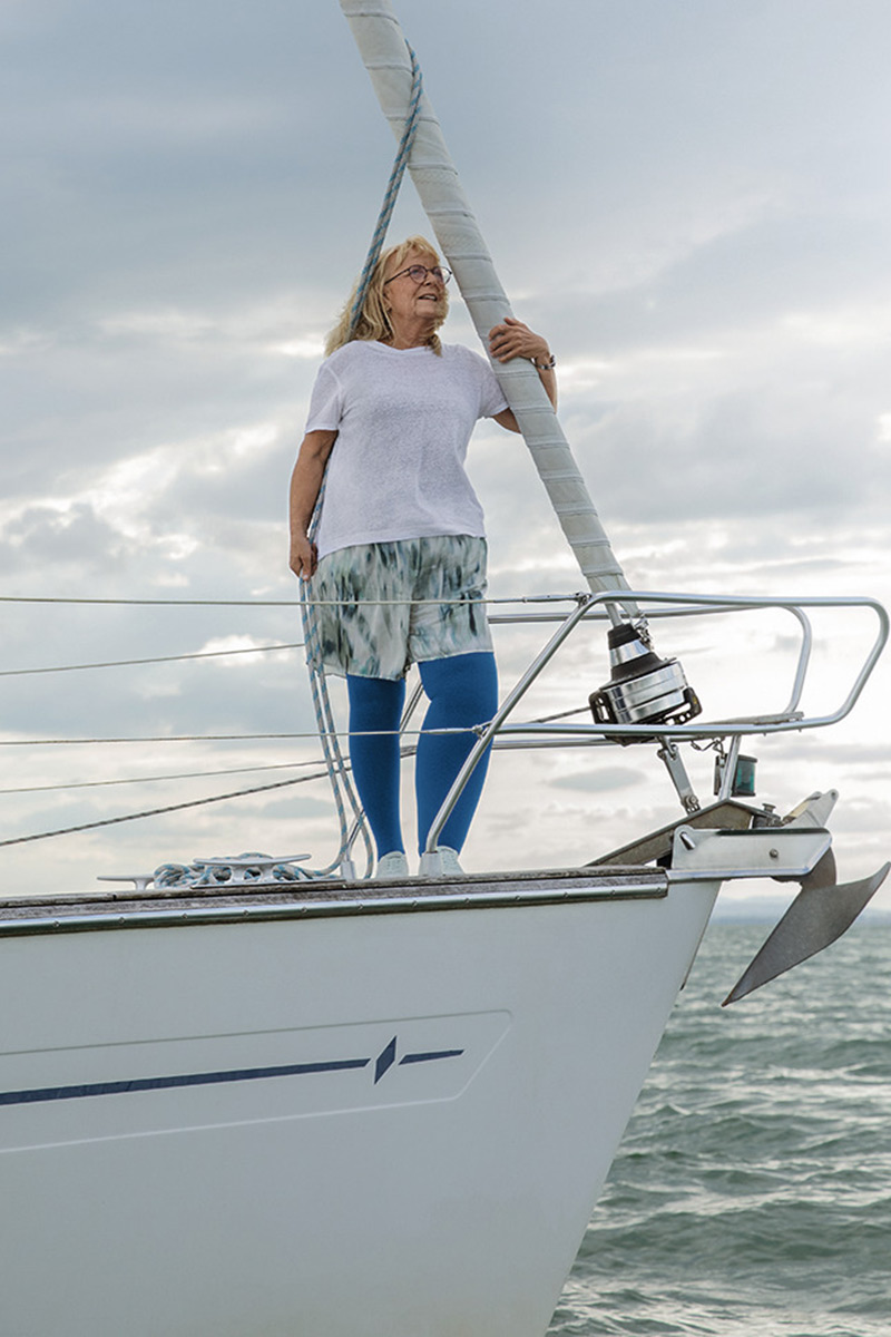 A woman is standing on a boat. She has lymphoedema in her leg and is wearing blue compression stockings
