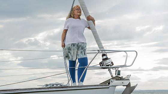 A woman with lymphoedema is standing on the deck of a boat. She is wearing blue compression stockings