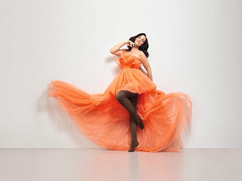 Mujer con vestido naranja. Lleva las medias marrones «Juzo Inspiration».