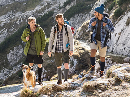 Three men with a dog in the mountains. The men are wearing compression stockings on their lower legs.